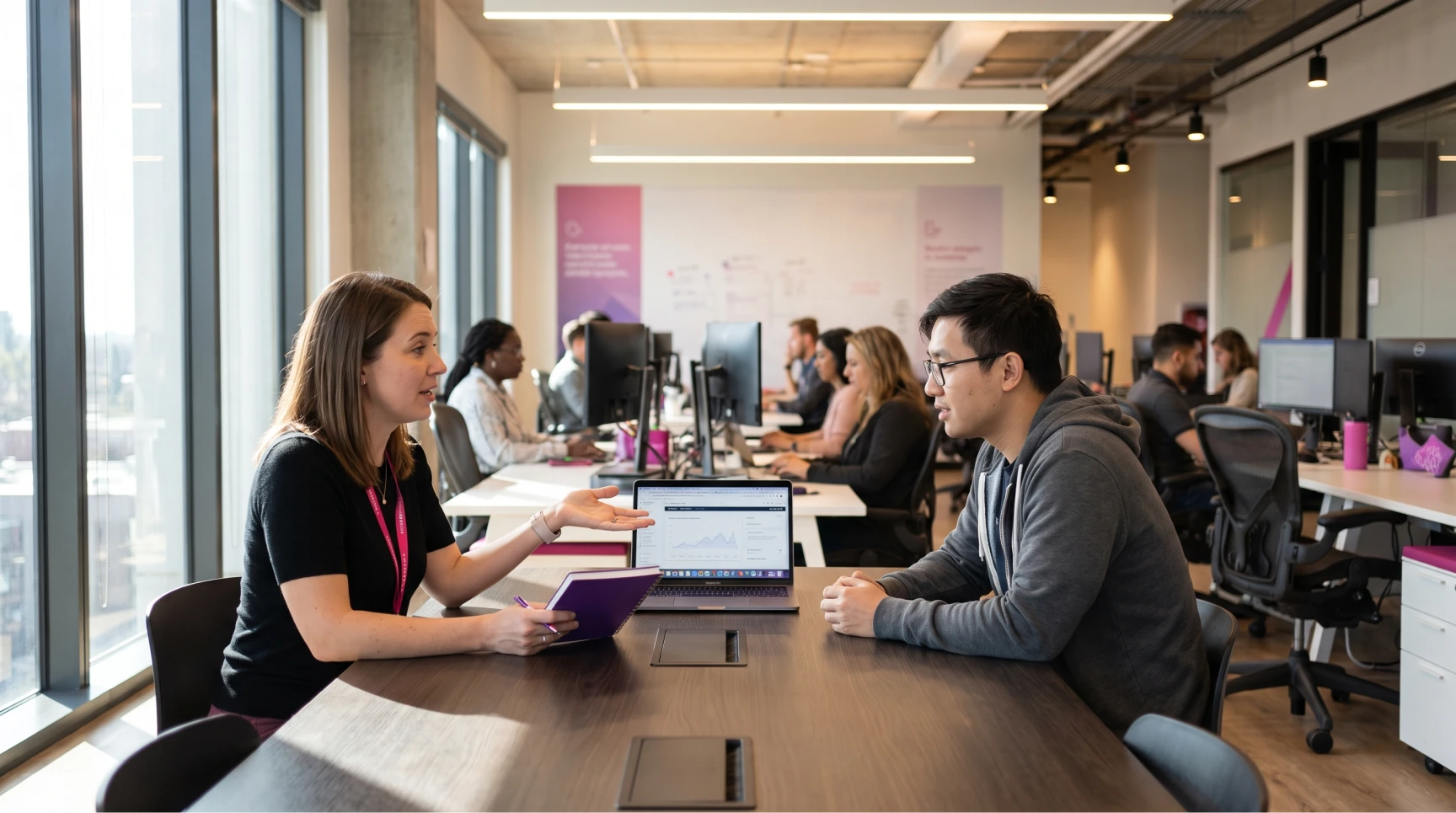 Uma profissional de talent acquisition de uma consultoria de recrutamento especializado conversa com um homem em potencial, possivelmente um desenvolvedor backend ou engenheiro de software, em uma mesa de conferência em um escritório moderno de plano aberto. A recrutadora explica dados em um laptop, ilustrando o processo seletivo e a estrutura de RH. No fundo, outros profissionais tech e membros de um time comercial SaaS trabalham, sugerindo uma cultura organizacional focada no crescimento acelerado. A cena representa o sourcing de candidatos para startups e o plano de contratação para reduzir o time to hire. Integre elementos de employer branding e recrutamento remoto.