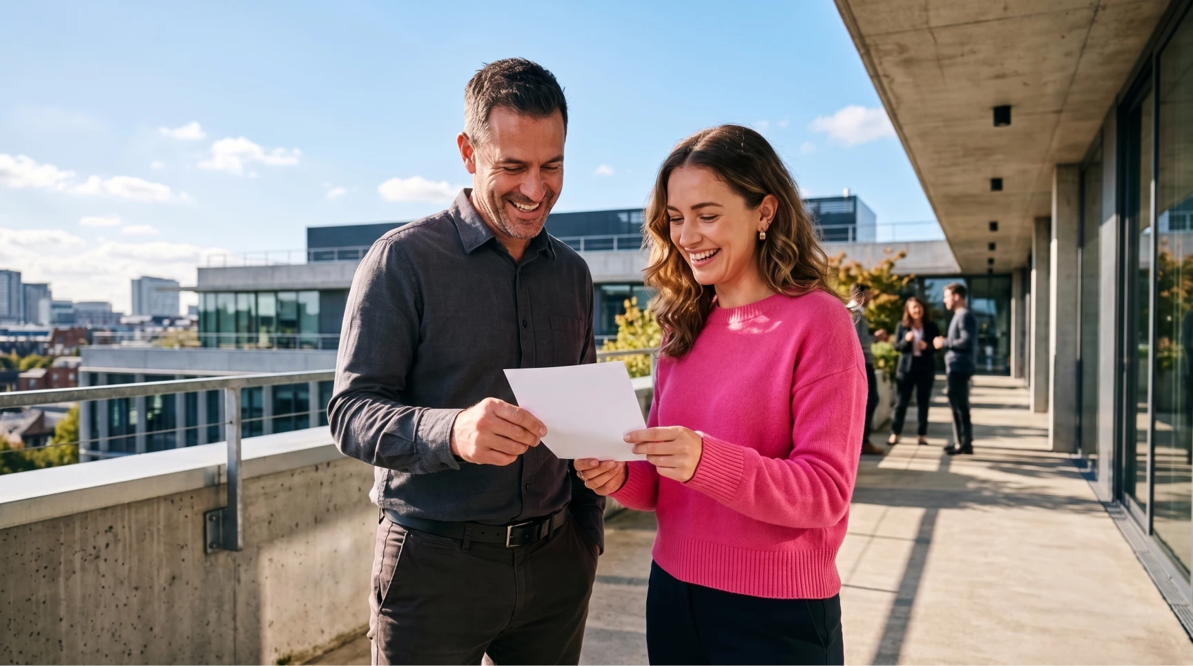 Um homem e uma mulher sorriem em uma varanda corporativa enquanto seguram e leem um documento impresso, simbolizando a eficiência e o dinamismo de um recrutamento ágil.