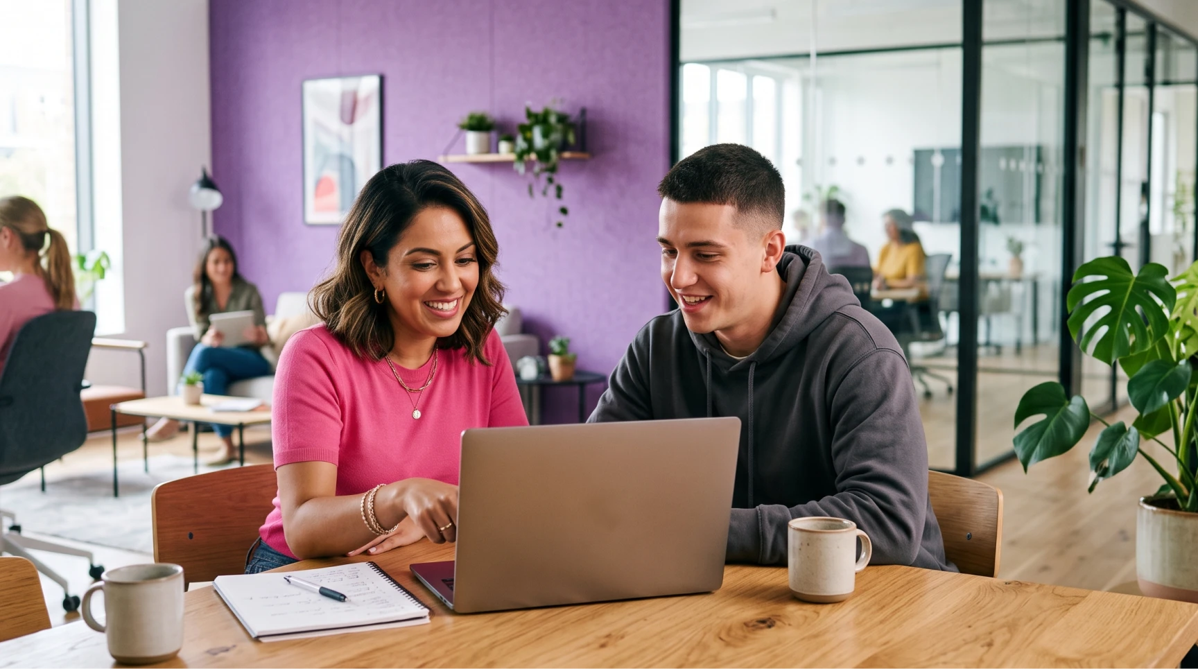 Uma mulher de camisa rosa e um jovem de moletom cinza sorriem sentados em frente a um laptop aberto, ilustrando a etapa de alinhamento e boas práticas na contratação de desenvolvedores.